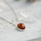  A playful 18" sterling silver necklace with a 10mm Baltic amber oval pendant on a light wood table, surrounded by soft decor. 
